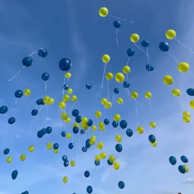 Bunte Luftballons in Blau und Gelb schweben am Himmel unter einem klaren blauen Himmel.