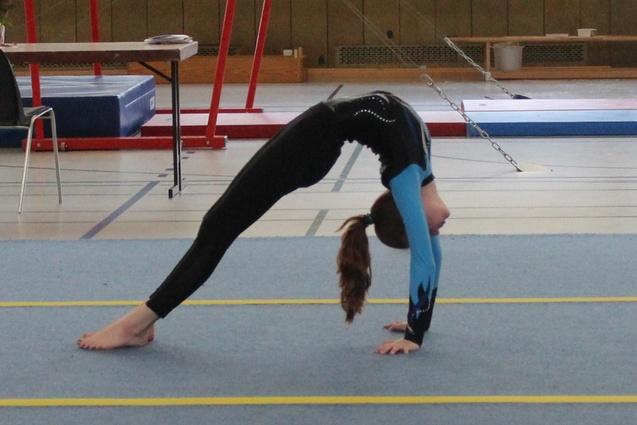 Mädchen in Sportkleidung macht eine Rückwärtsbrücke auf einem blauen Turnboden in einer Turnhalle.