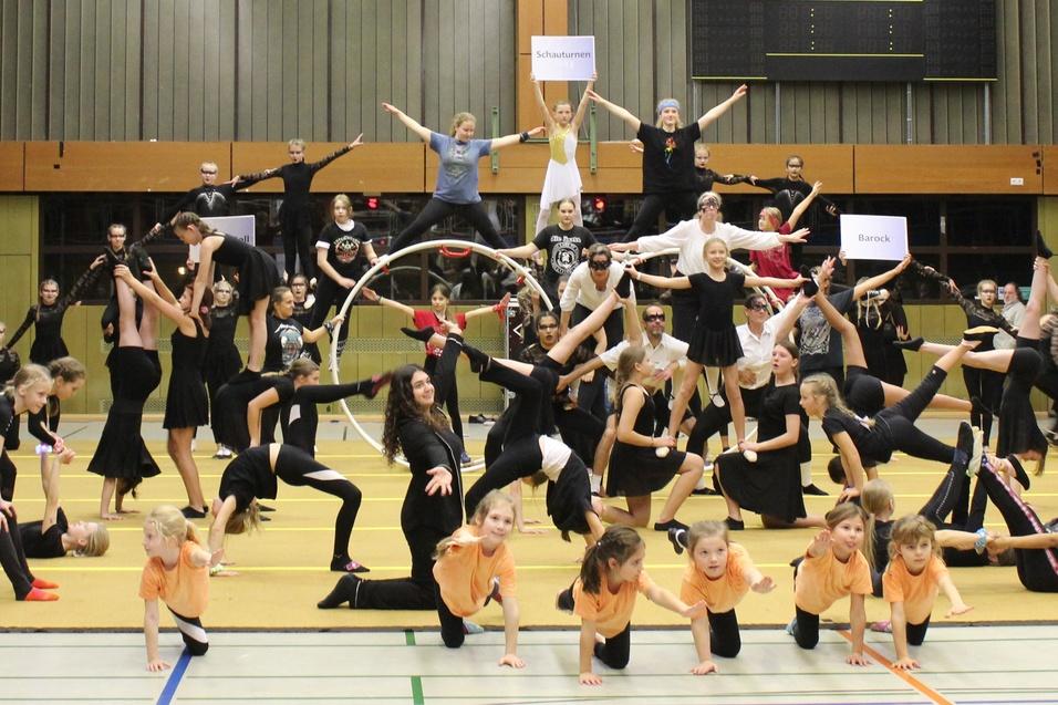 Gruppendarstellung von Kindern und Jugendlichen in unterschiedlichen Posen w&auml;hrend einer Akrobatikvorf&uuml;hrung in einer Halle.