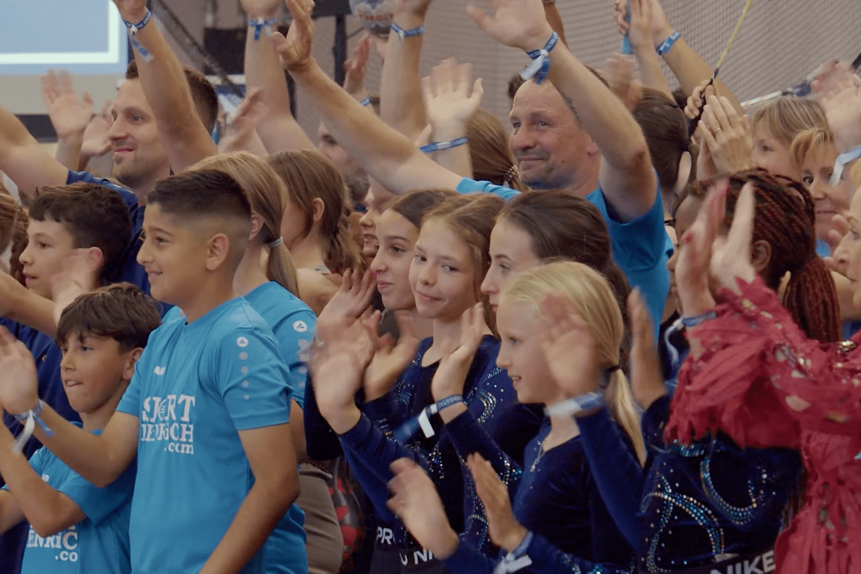 Gruppe von Kindern und Erwachsenen in blauen T-Shirts, die begeistert applaudieren und lächeln.