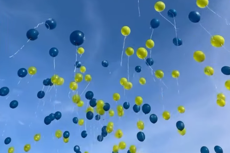 Bunte Luftballons in Blau und Gelb schweben am Himmel unter einem klaren blauen Himmel.