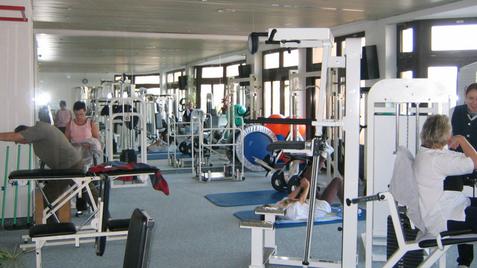 Fitnessstudio mit mehreren Trainingsgeräten und Personen, die unterschiedliche Übungen durchführen. Helle, helle Umgebung.