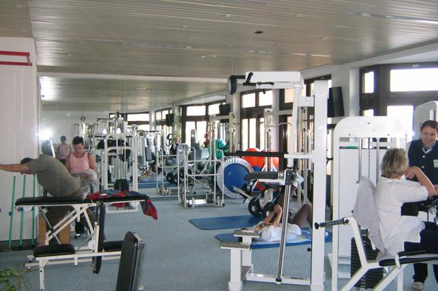 Fitnessstudio mit mehreren Trainingsger&auml;ten und Personen, die unterschiedliche &Uuml;bungen durchf&uuml;hren. Helle, helle Umgebung.