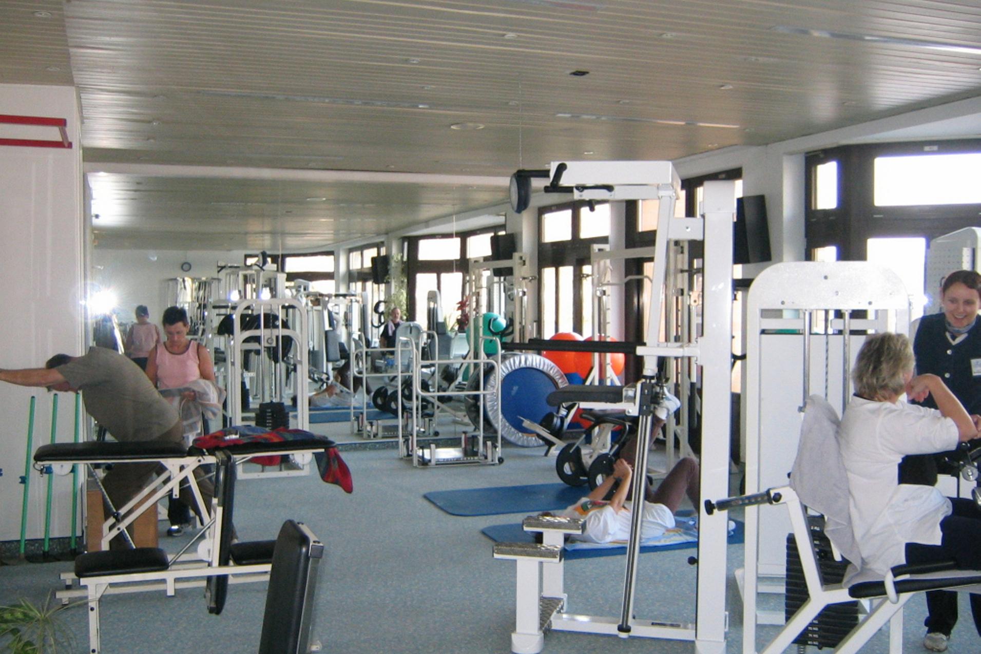 Fitnessstudio mit mehreren Trainingsger&auml;ten und Personen, die unterschiedliche &Uuml;bungen durchf&uuml;hren. Helle, helle Umgebung.