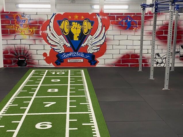 Fitnessstudio mit einem grünen Wettkampfbereich, Wänden mit Graffiti und einer freistehenden Trainingsstation.