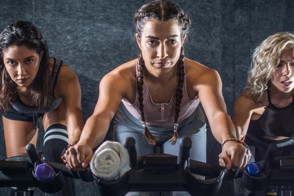Drei Frauen konzentrieren sich beim Indoor-Cycling in einem modernen Fitnessstudio.