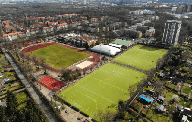 Luftaufnahme eines Sportgel&auml;ndes mit verschiedenen Sportfeldern, darunter eine Laufbahn, Fu&szlig;ball- und Tennispl&auml;tze.