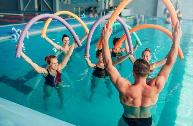 Gruppe von Frauen und einem Mann im Wasser mit Schwimmnudeln während einer Aquafitness-Stunde.