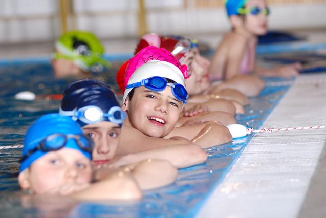 Gruppe von Kindern in Schwimmbekleidung, die an einem Schwimmbeckenrand entspannen und lächeln.