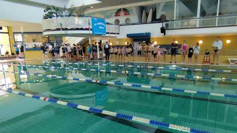 Schwimmbecken mit mehreren Bahnen und zahlreichen wartenden Schwimmern am Rand des Pools in einem Hallenbad.