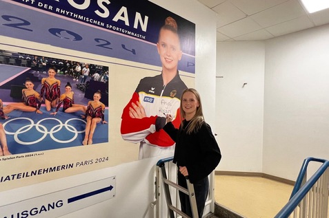 Junge Frau steht an einer Wand mit einem Plakat von Anja Kosan, bevor sie an den Olympischen Spielen 2024 teilnehmen.