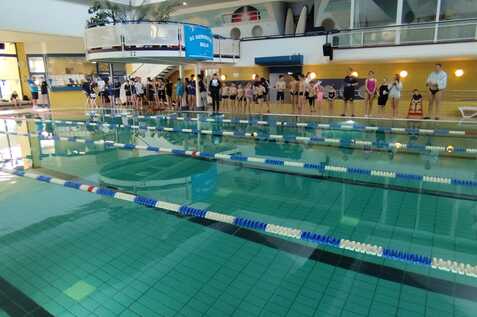 Schwimmbecken mit mehreren Bahnen und zahlreichen wartenden Schwimmern am Rand des Pools in einem Hallenbad.