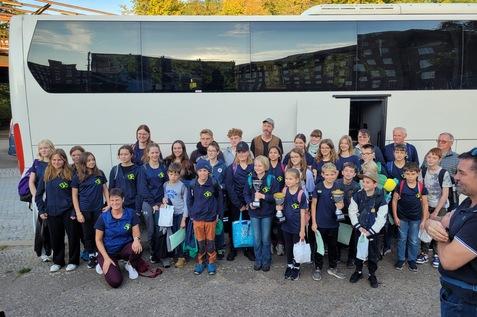 Gruppe von Kindern und Erwachsenen in Sportkleidung vor einem Reisebus, einige halten Pokale in den H&auml;nden.