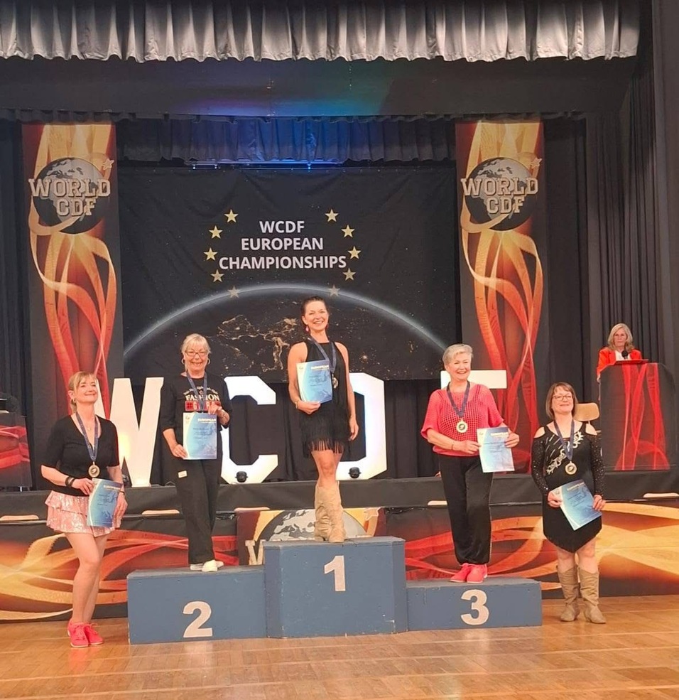 Fünf Tänzerinnen stehen auf dem Siegertreppchen bei den WCDF European Championships, Urkunden in der Hand.