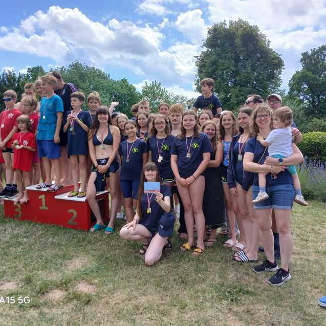 Gruppe von Kindern und Jugendlichen in Badebekleidung, posierend auf einem Siegertreppchen nach einem Wettkampf.