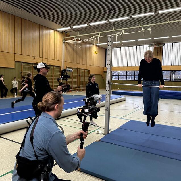 Person beim Training an einem Reck in einer Sporthalle, w&auml;hrend Videoaufnahmen durchgef&uuml;hrt werden.