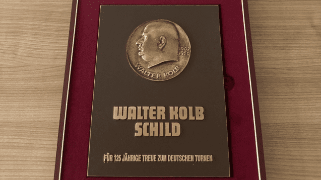 Bronzeplakette mit Inschrift „Walter Kolb Schild“ zur Ehrung für 125 Jahre Treue zum Deutschen Turnen in einer Präsentationsbox.