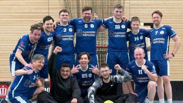 Gruppennfoto einer Handballmannschaft in blauen Trikots, lächelnd und posierend in einer Sporthalle.