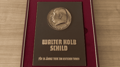 Bronzeplakette mit Inschrift „Walter Kolb Schild“ zur Ehrung für 125 Jahre Treue zum Deutschen Turnen in einer Präsentationsbox.