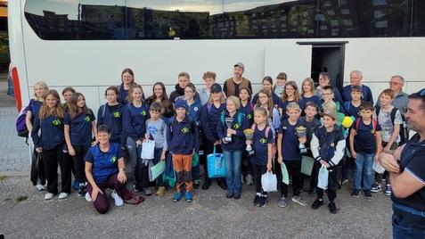 Gruppe von Kindern und Erwachsenen in Sportkleidung vor einem Reisebus, einige halten Pokale in den Händen.