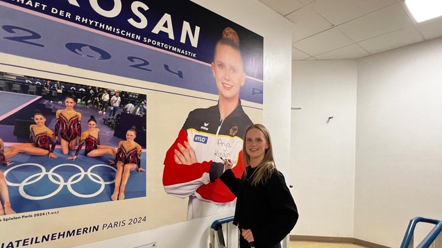 Junge Frau steht an einer Wand mit einem Plakat von Anja Kosan, bevor sie an den Olympischen Spielen 2024 teilnehmen.