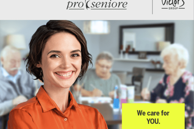 L&auml;chelnde Frau mit kurzer Frisur tr&auml;gt ein oranges Hemd, w&auml;hrend im Hintergrund Senioren an einem Tisch aktiv sind.