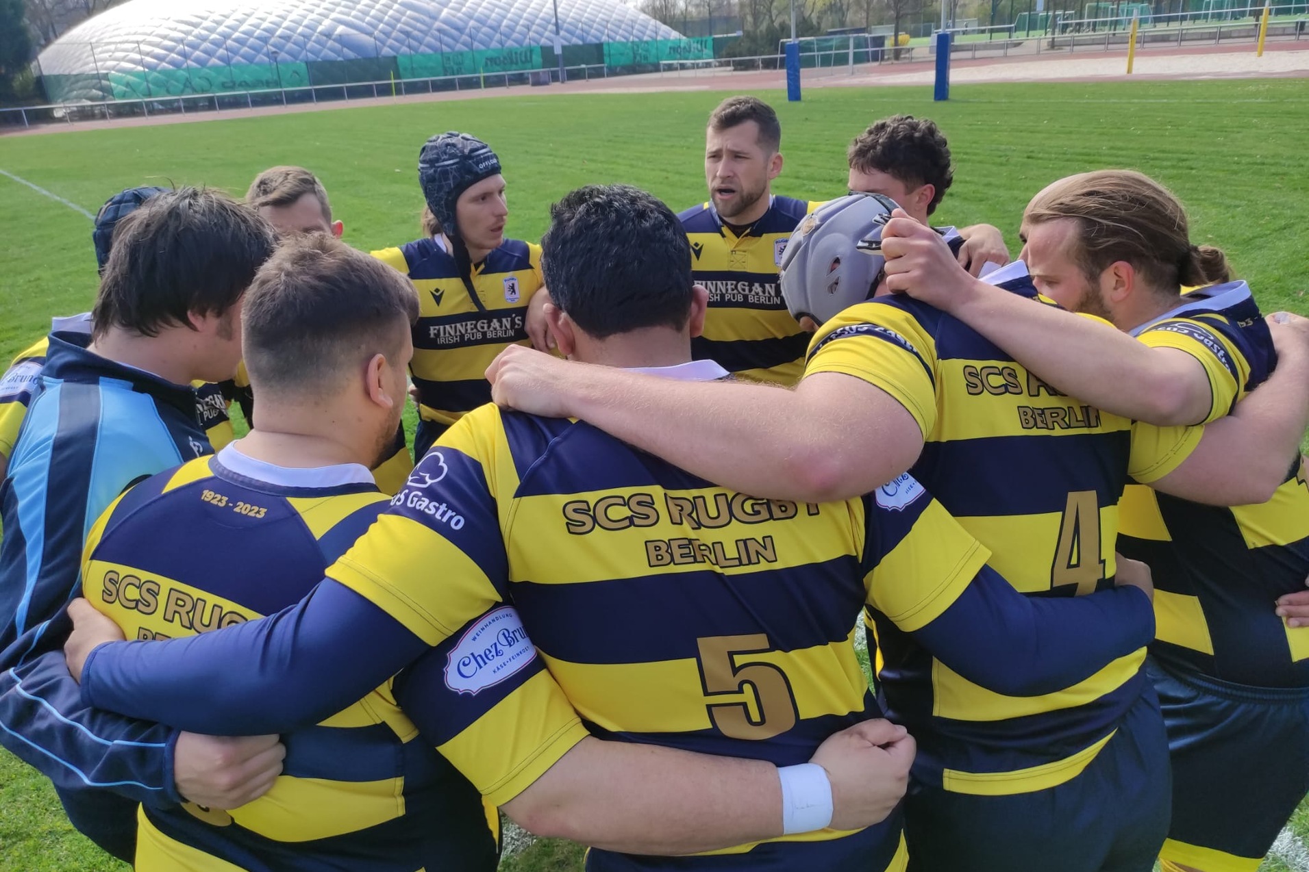 Rugby-Mannschaft in schwarz-gelben Trikots bildet einen Kreis auf dem Spielfeld und bespricht sich vor dem Spiel.