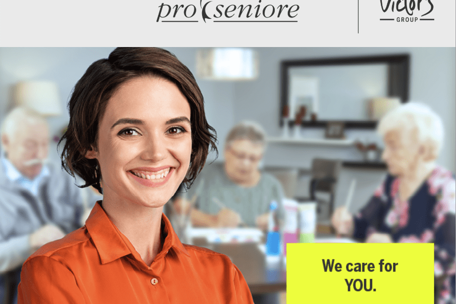 L&auml;chelnde Frau mit kurzer Frisur tr&auml;gt ein oranges Hemd, w&auml;hrend im Hintergrund Senioren an einem Tisch aktiv sind.