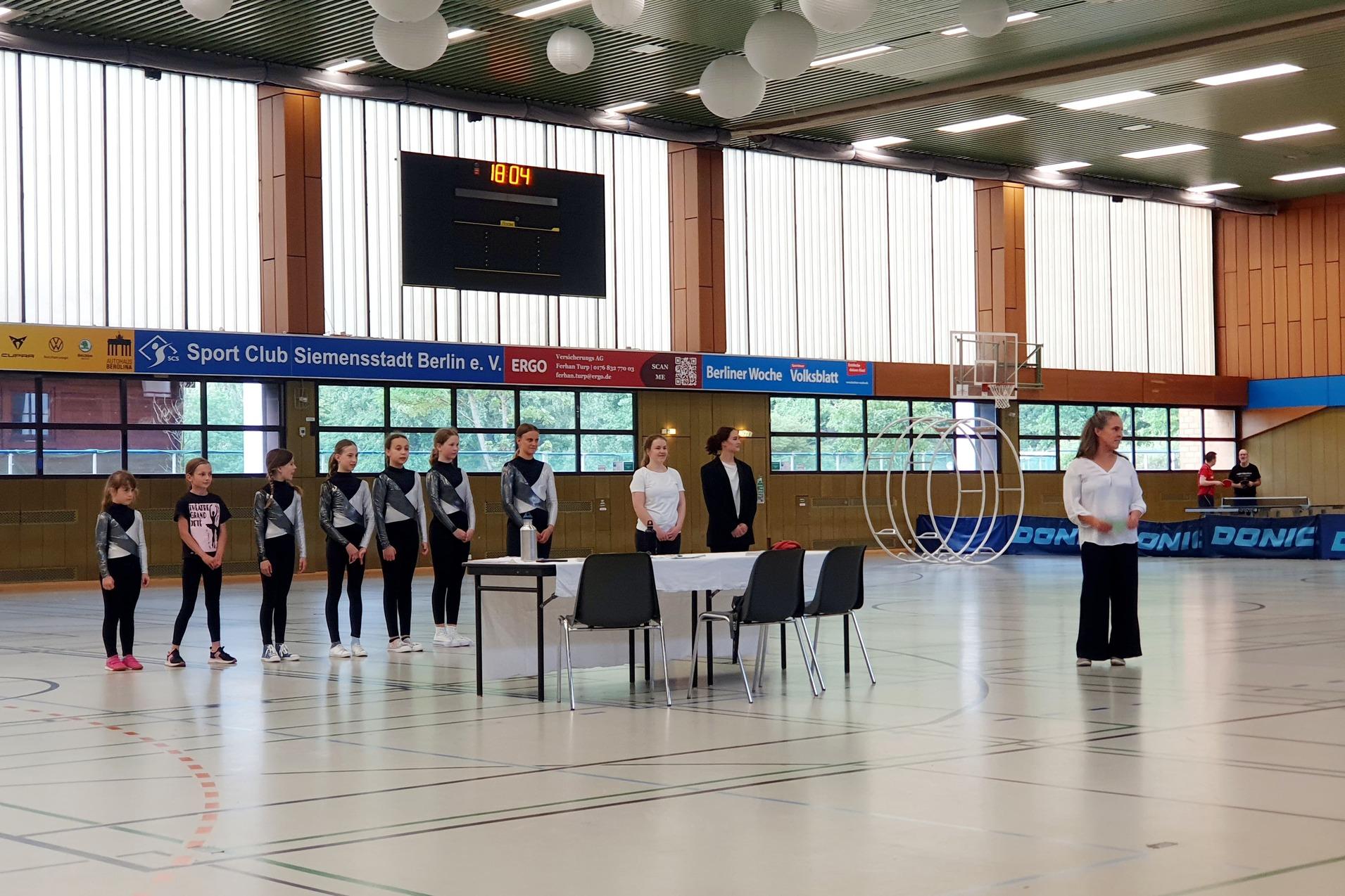 Gruppendouzierung von Sportlerinnen in Wettkampfkleidung w&auml;hrend einer Veranstaltung in einer Sporthalle.