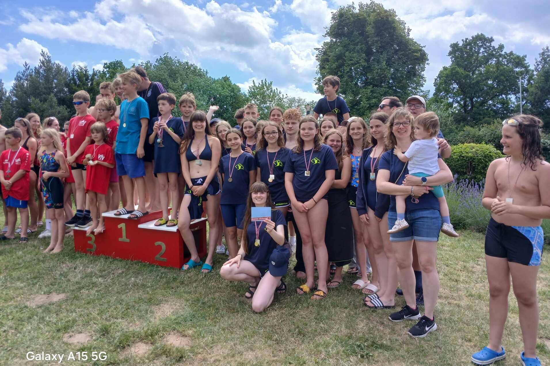Gruppe von Kindern und Jugendlichen in Badebekleidung, posierend auf einem Siegertreppchen nach einem Wettkampf.
