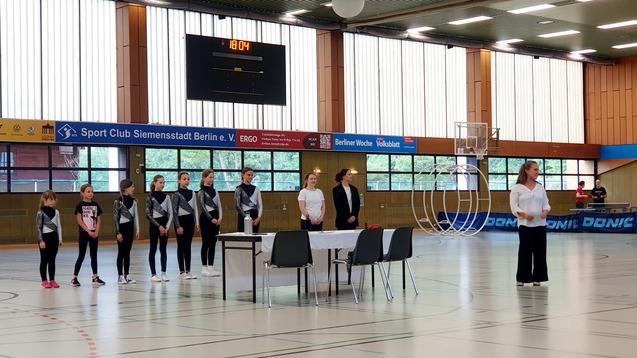 Gruppendouzierung von Sportlerinnen in Wettkampfkleidung während einer Veranstaltung in einer Sporthalle.