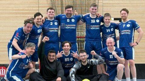 Gruppennfoto einer Handballmannschaft in blauen Trikots, lächelnd und posierend in einer Sporthalle.