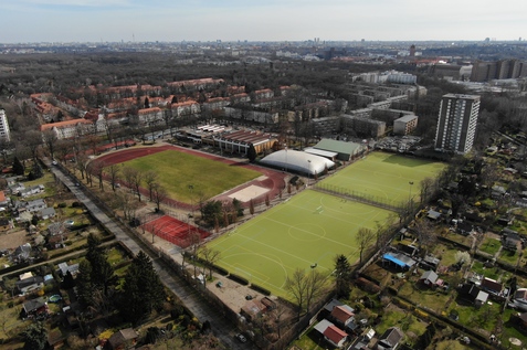 Luftaufnahme eines Sportgel&auml;ndes mit Tennispl&auml;tzen, Fu&szlig;ballfeld und Wohngeb&auml;uden in der Umgebung.