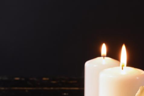 Zwei brennende, wei&szlig;e Kerzen stehen vor einem dunklen Hintergrund.