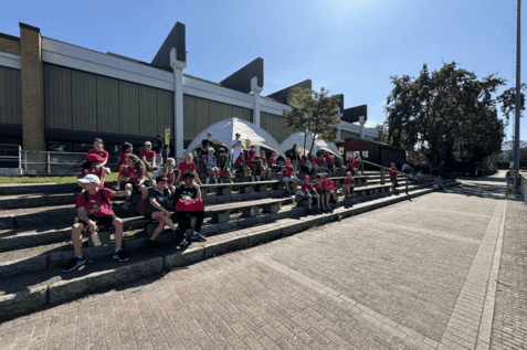 Gruppenbild von Kindern in roten T-Shirts, die auf B&auml;nken sitzen