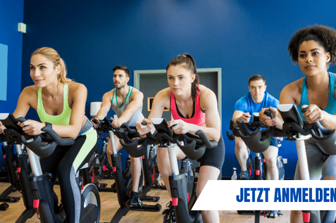 Gruppe von Personen in einem Fitnesskurs, die auf Spinning-R&auml;dern trainieren, mit Anmeldehinweis im Vordergrund.