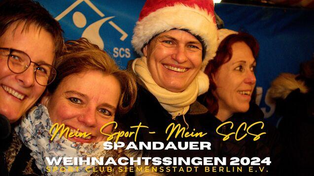 F&uuml;nf Frauen l&auml;cheln fr&ouml;hlich mit Weihnachtsm&uuml;tzen vor einem blauen Hintergrund beim Weihnachtssingen.