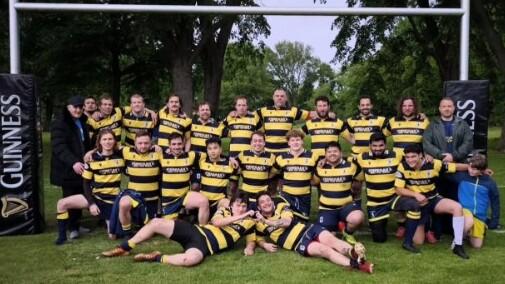Gruppenshot von Rugbyspielern in gestreiften Trikots vor einem Rugbytor mit Guinness-Werbepylonen im Hintergrund.