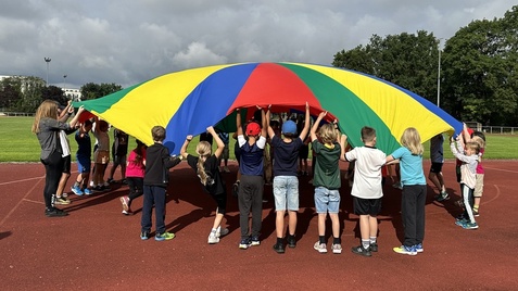 Kinder, die ein buntes Schwungtuch hochhalten