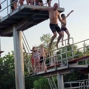 Gruppenspringer auf einem Sprungbrett, w&auml;hrend andere Schwimmer am Beckenrand warten. Sommerliche Atmosph&auml;re im Freibad.