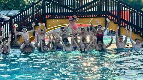 Gruppenshot von Kindern und Erwachsenen im Wasser, die fröhlich mit erhobenen Händen posieren, im Hintergrund eine Rutsche.