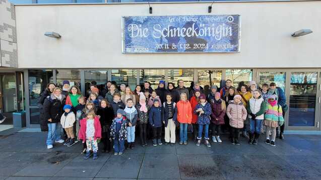 Gruppe von Kindern und Erwachsenen steht vor einem Gebäude mit Plakat für „Die Schneekönigin“, ein Tanzprojekt.