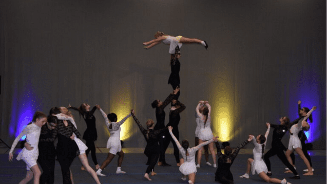 Tanzgruppe führt akrobatische Elemente auf, mit einer Tänzerin in der Luft über mehreren anderen Tänzern.