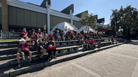 Gruppenbild von Kindern in roten T-Shirts, die auf Bänken sitzen