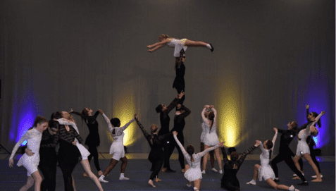 Tanzgruppe führt akrobatische Elemente auf, mit einer Tänzerin in der Luft über mehreren anderen Tänzern.