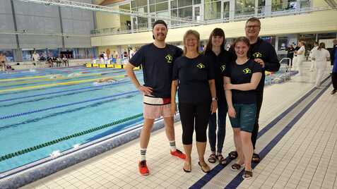 Gruppe von fünf Schwimmern in Vereinskleidung steht am Beckenrand eines Schwimmbeckens während eines Wettkampfs.