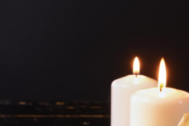 Zwei brennende, wei&szlig;e Kerzen stehen vor einem dunklen Hintergrund.