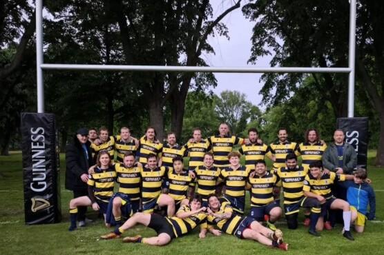 Gruppenshot von Rugbyspielern in gestreiften Trikots vor einem Rugbytor mit Guinness-Werbepylonen im Hintergrund.
