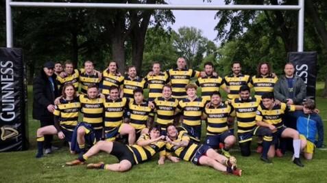 Gruppenshot von Rugbyspielern in gestreiften Trikots vor einem Rugbytor mit Guinness-Werbepylonen im Hintergrund.