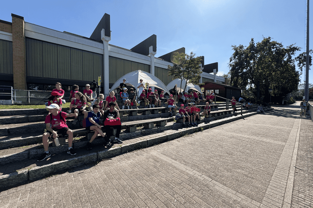 Gruppenbild von Kindern in roten T-Shirts, die auf B&auml;nken sitzen